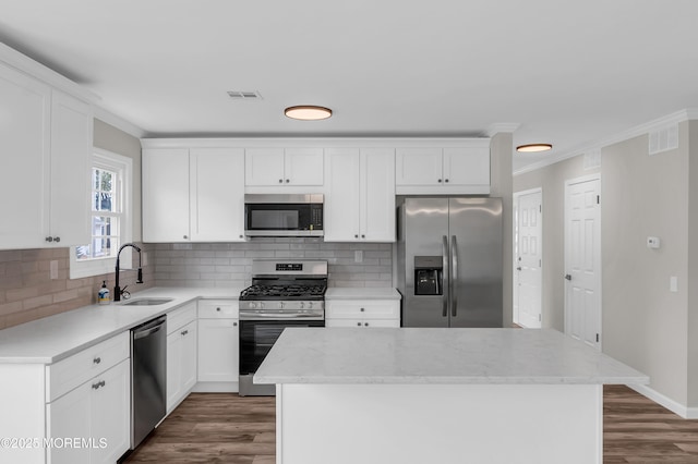 kitchen with stainless steel appliances, white cabinets, a kitchen island, and a sink