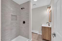 bathroom featuring a tile shower, vanity, and baseboards