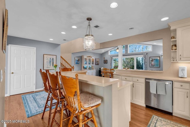 kitchen featuring a breakfast bar area, light hardwood / wood-style floors, dishwasher, white cabinetry, and pendant lighting