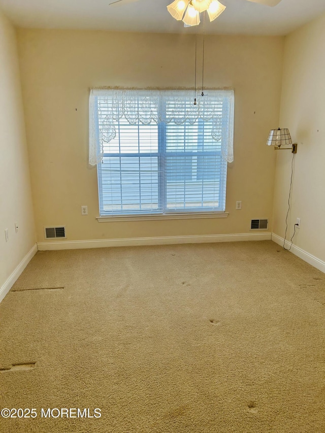 empty room with ceiling fan, carpet floors, visible vents, and baseboards