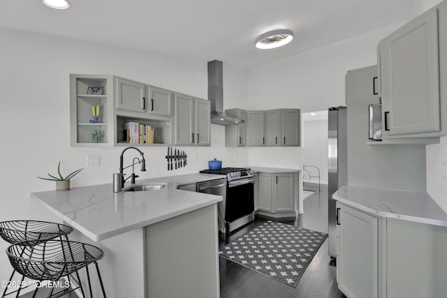 kitchen with wall chimney exhaust hood, appliances with stainless steel finishes, a peninsula, gray cabinets, and open shelves