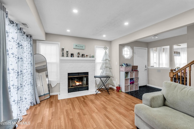 living area featuring baseboards, stairway, wood finished floors, a brick fireplace, and recessed lighting