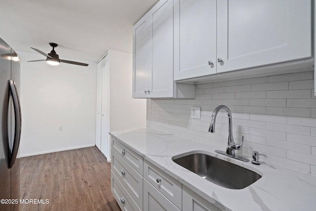 kitchen with white cabinets, sink, black fridge, and light stone counters