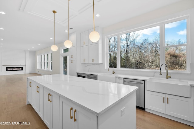 kitchen with stainless steel dishwasher, sink, white cabinetry, and light stone countertops