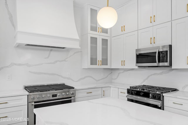 kitchen with appliances with stainless steel finishes, hanging light fixtures, white cabinets, decorative backsplash, and custom exhaust hood