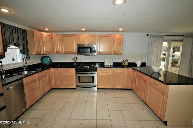 kitchen featuring dark stone countertops, light tile patterned floors, stainless steel appliances, a sink, and decorative backsplash