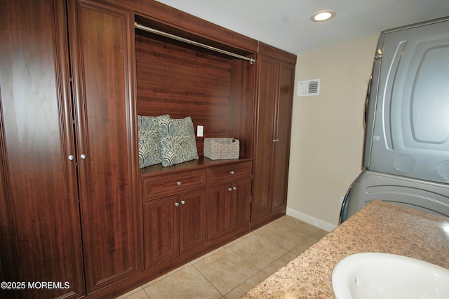 bathroom featuring baseboards, visible vents, vanity, tile patterned flooring, and stacked washing maching and dryer