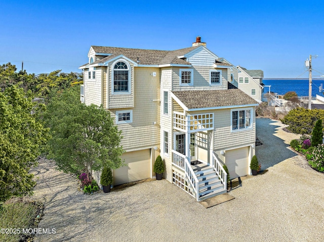 view of front of house with a garage, a shingled roof, a water view, driveway, and a chimney