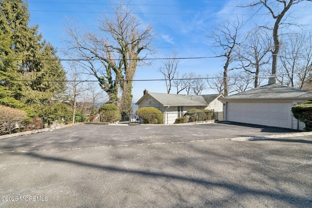 view of front of house featuring an outbuilding, a chimney, a detached garage, and fence