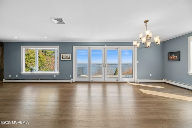 spare room featuring baseboards, visible vents, wood finished floors, an inviting chandelier, and a baseboard heating unit