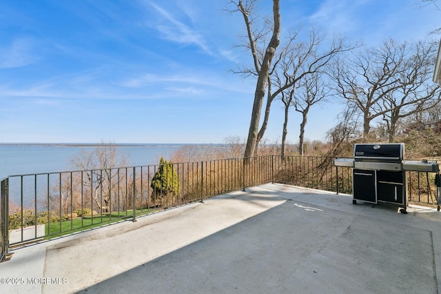 view of patio featuring grilling area, fence, and a water view