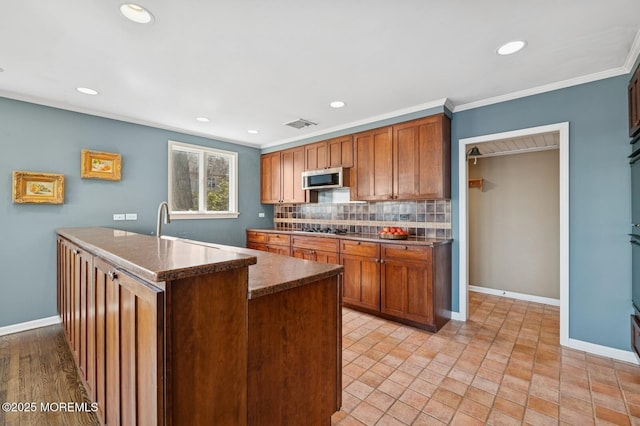 kitchen with tasteful backsplash, stainless steel microwave, baseboards, and ornamental molding