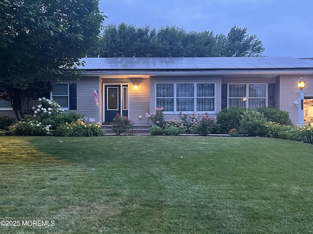 single story home with roof mounted solar panels, entry steps, and a front lawn