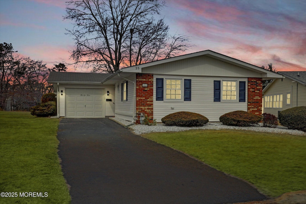ranch-style house with an attached garage, aphalt driveway, and a lawn