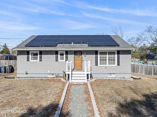 ranch-style house with fence, solar panels, and roof with shingles