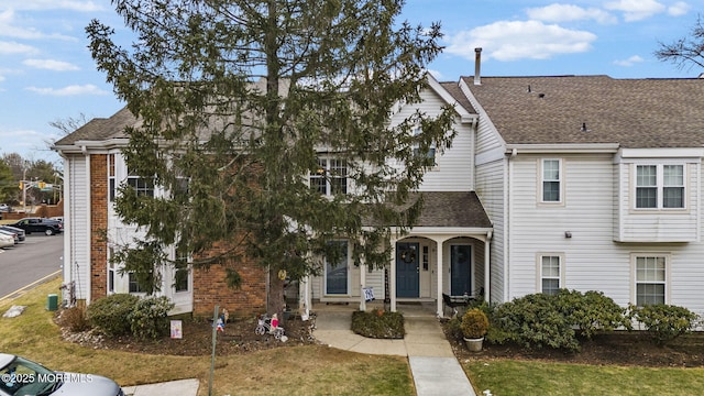 townhome / multi-family property with roof with shingles, brick siding, and a front lawn