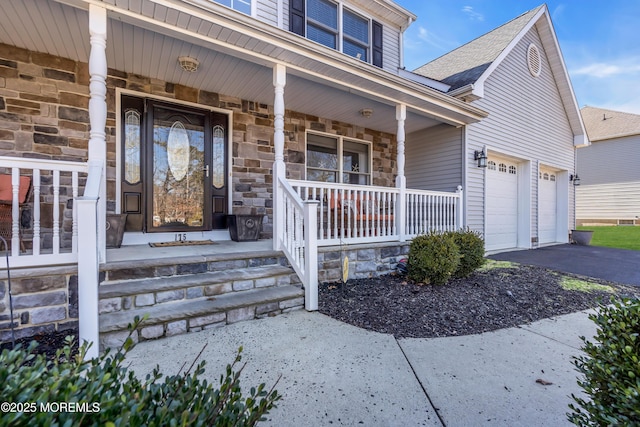 property entrance with covered porch, stone siding, an attached garage, and driveway