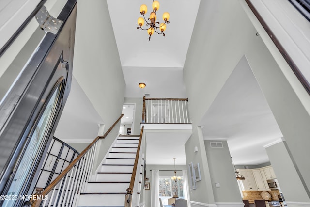 foyer with a notable chandelier, visible vents, stairway, a high ceiling, and ornamental molding