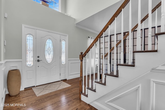 entryway with wainscoting, stairway, wood finished floors, a high ceiling, and a decorative wall