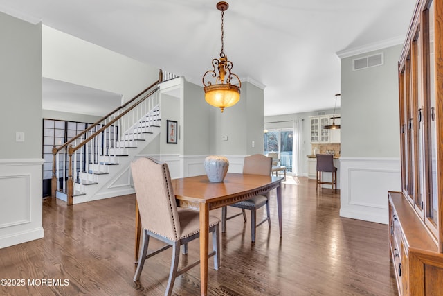 dining room with a decorative wall, dark wood-type flooring, visible vents, stairway, and crown molding