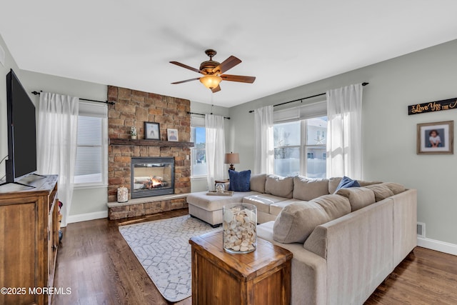 living room featuring visible vents, baseboards, dark wood finished floors, a ceiling fan, and a fireplace