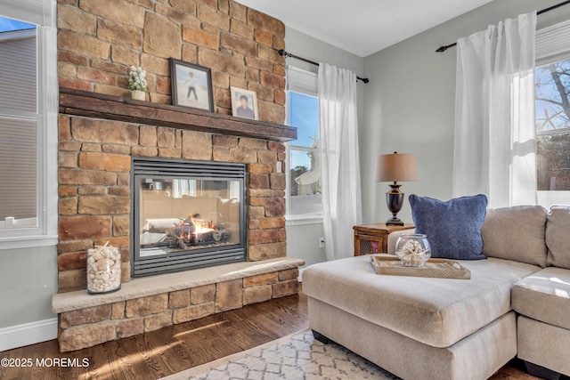 living area with baseboards, wood finished floors, and a stone fireplace