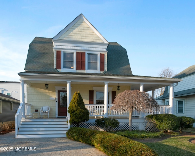 view of front facade with roof with shingles, a porch, and a gambrel roof