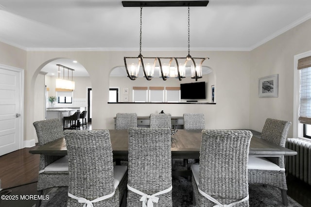 dining space featuring arched walkways, ornamental molding, radiator heating unit, and wood finished floors