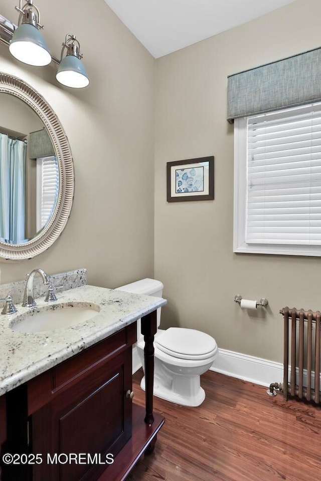 bathroom featuring baseboards, toilet, radiator heating unit, wood finished floors, and vanity