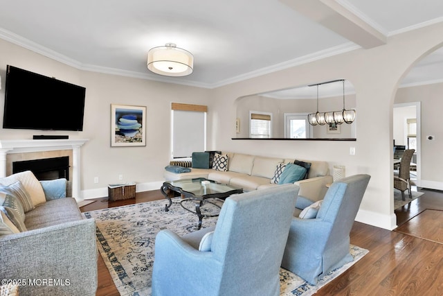 living area featuring arched walkways, a fireplace, wood finished floors, baseboards, and crown molding