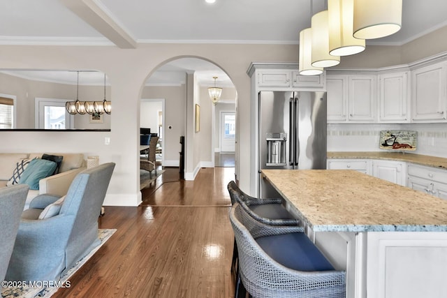 kitchen with arched walkways, dark wood-style floors, light stone counters, ornamental molding, and high end fridge