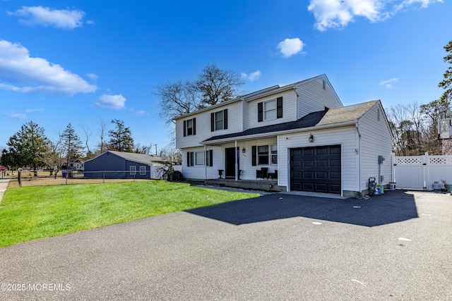 colonial home featuring a porch, aphalt driveway, an attached garage, fence, and a front lawn