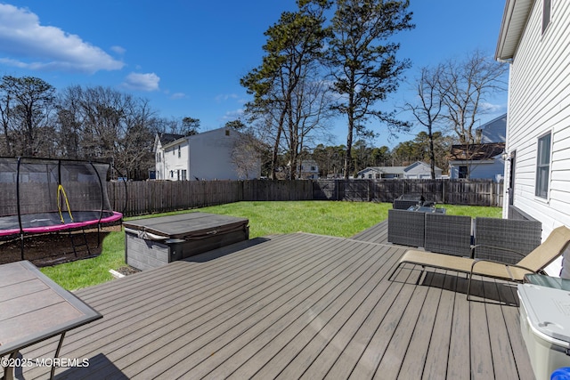 wooden terrace with a lawn, a fenced backyard, a residential view, a covered hot tub, and a trampoline