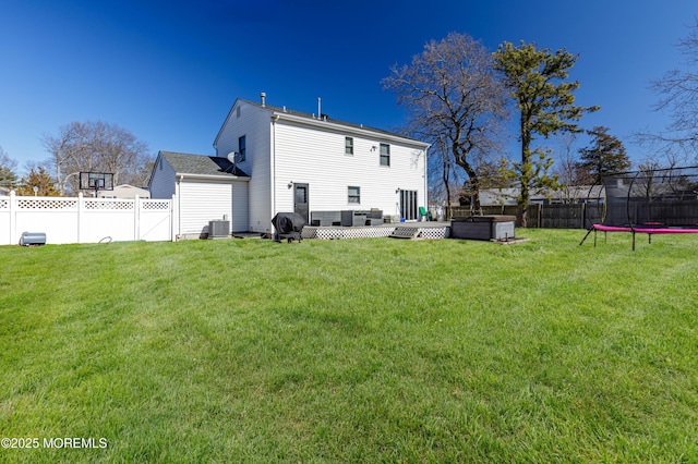 rear view of house featuring a hot tub, a trampoline, cooling unit, and a fenced backyard