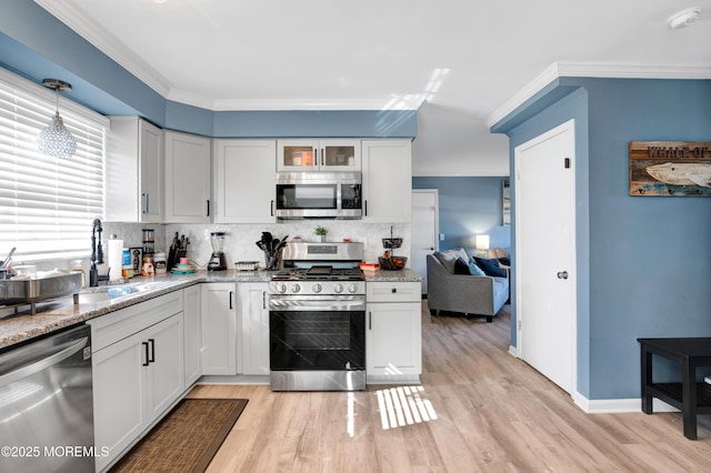 kitchen featuring decorative light fixtures, white cabinets, appliances with stainless steel finishes, glass insert cabinets, and crown molding