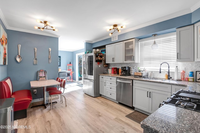 kitchen with glass insert cabinets, appliances with stainless steel finishes, light stone counters, hanging light fixtures, and crown molding