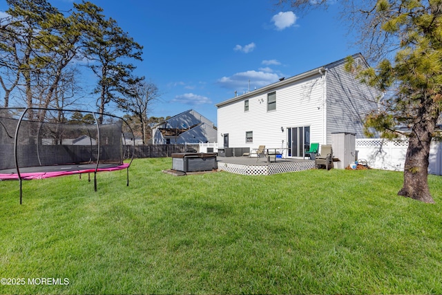 rear view of property with a yard, a fenced backyard, a trampoline, and a wooden deck