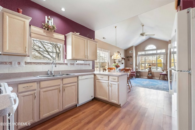 kitchen with a peninsula, white appliances, a sink, light countertops, and pendant lighting