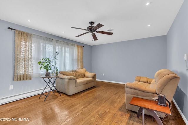 sitting room with a baseboard heating unit, wood finished floors, visible vents, a ceiling fan, and baseboards