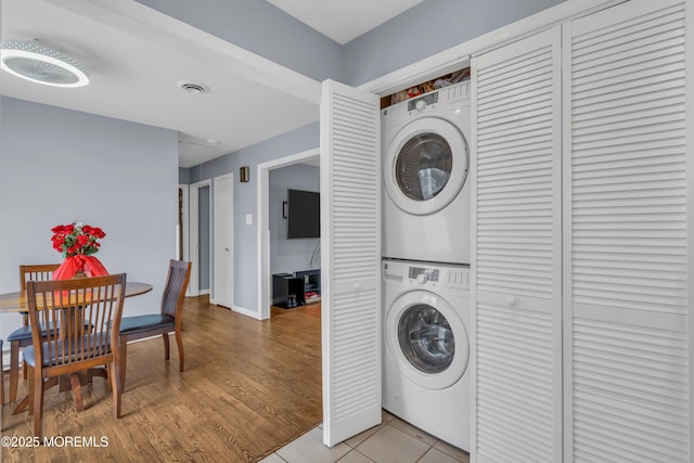 laundry area featuring laundry area, baseboards, visible vents, stacked washer / drying machine, and light wood-style floors