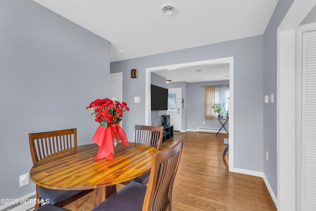 dining area featuring light wood-type flooring, a baseboard radiator, visible vents, and baseboards