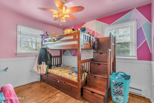 bedroom with a wainscoted wall, multiple windows, and wood finished floors