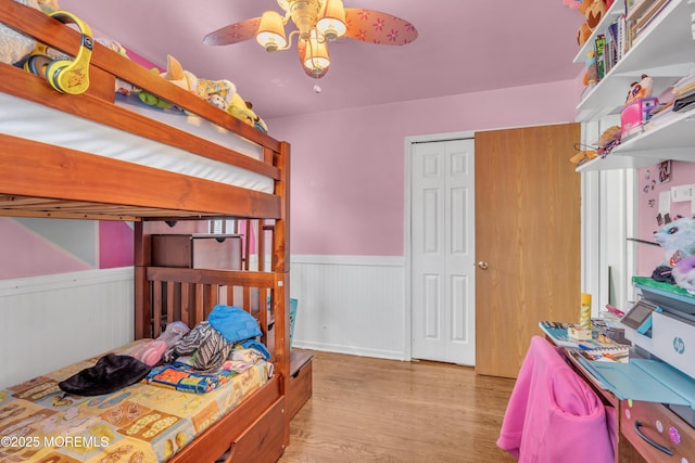 bedroom with a closet, wainscoting, ceiling fan, and light wood finished floors