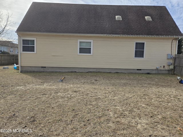 rear view of house featuring roof with shingles, crawl space, and fence