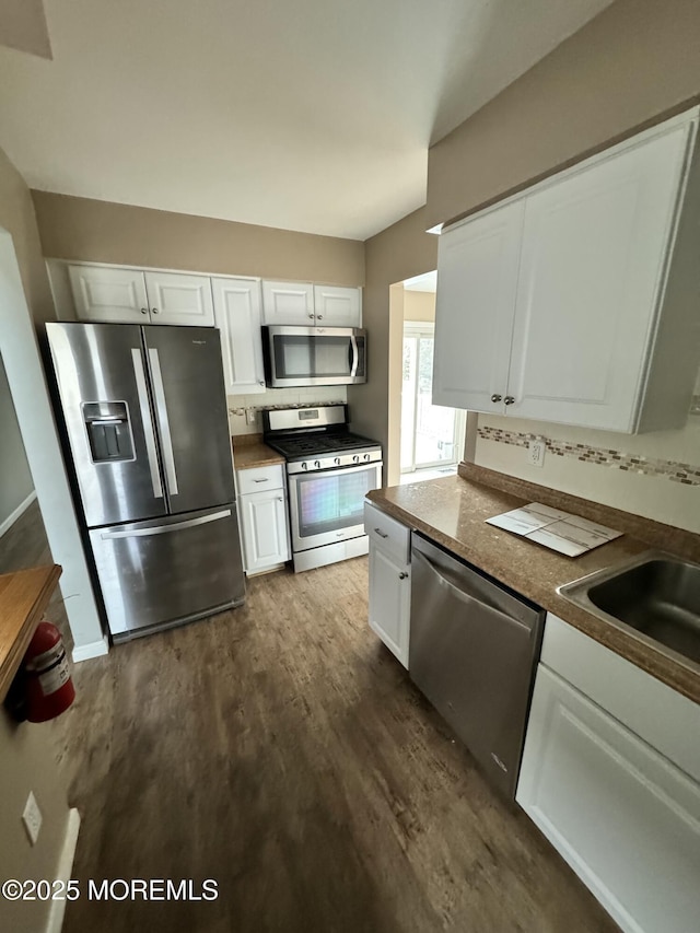 kitchen featuring dark countertops, appliances with stainless steel finishes, dark wood-type flooring, white cabinetry, and a sink