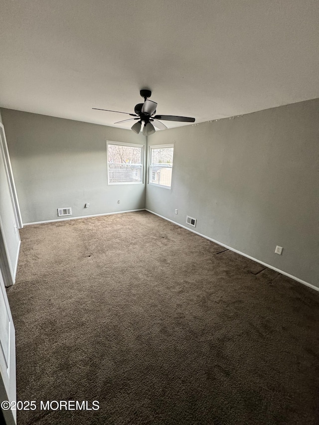 empty room with visible vents, dark carpet, and a ceiling fan