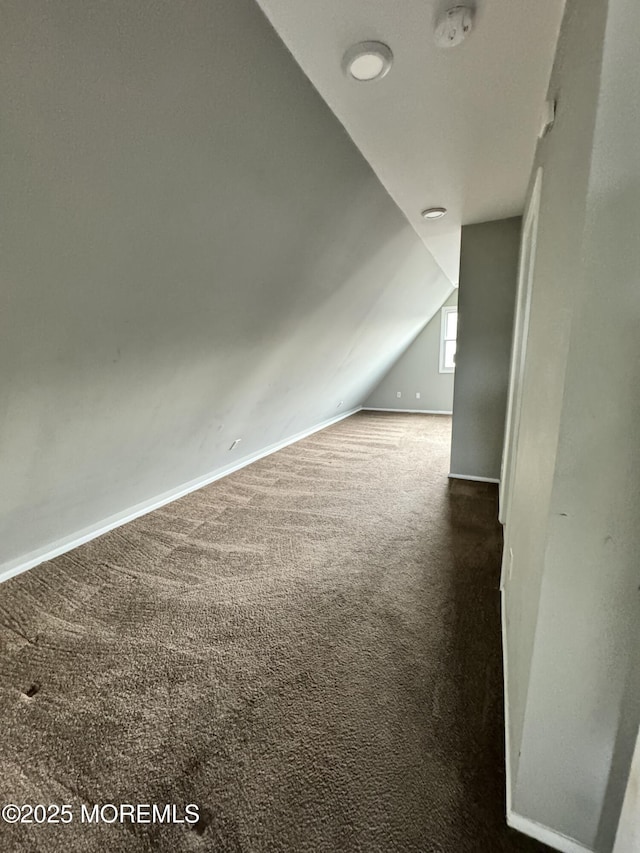 additional living space featuring lofted ceiling, dark colored carpet, and baseboards