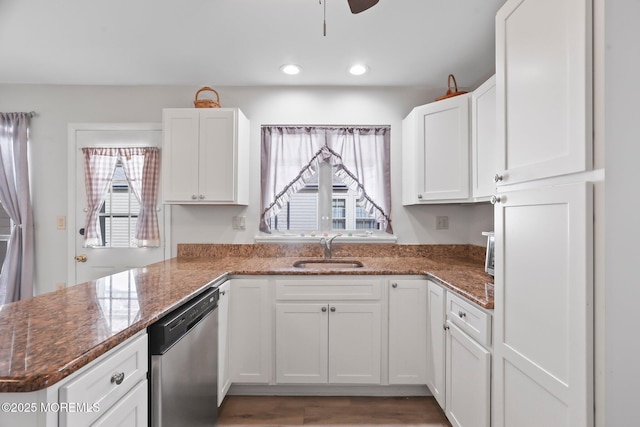 kitchen featuring dark stone countertops, a peninsula, stainless steel dishwasher, white cabinetry, and a sink