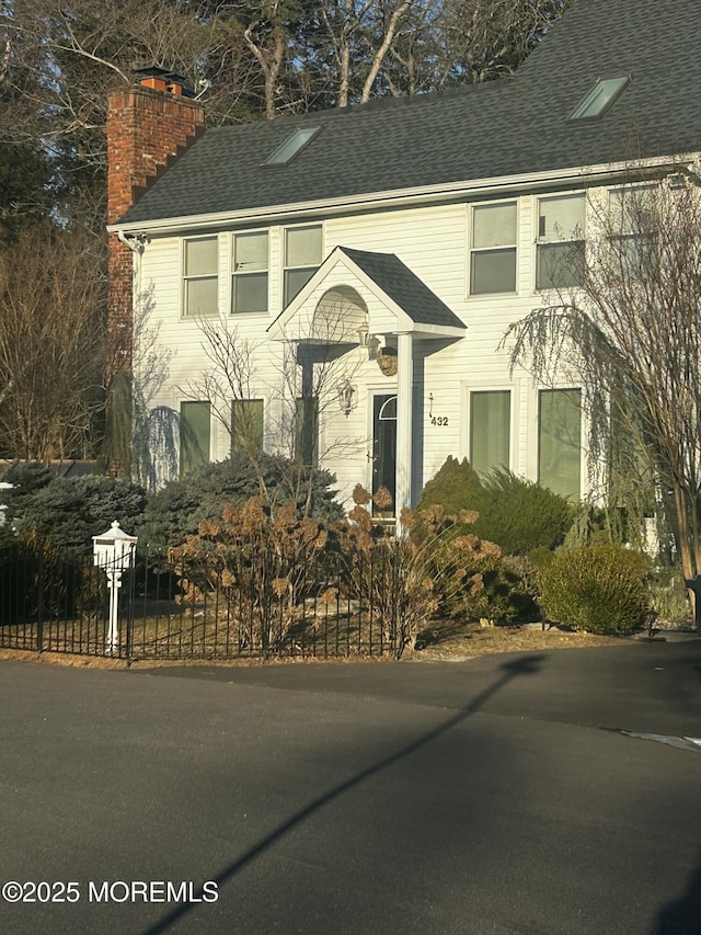 view of front of home with roof with shingles, a chimney, and fence