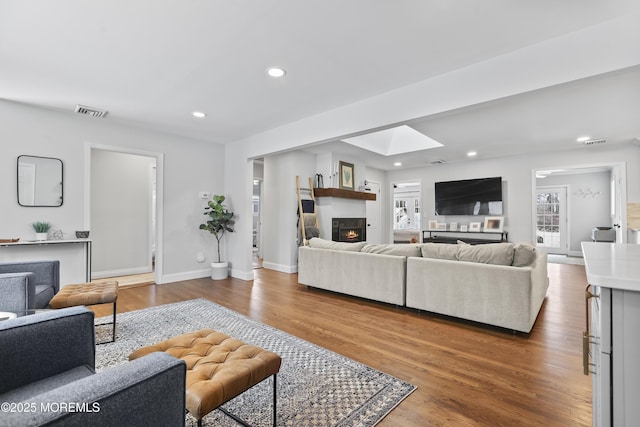 living area with recessed lighting, a skylight, wood finished floors, visible vents, and a lit fireplace